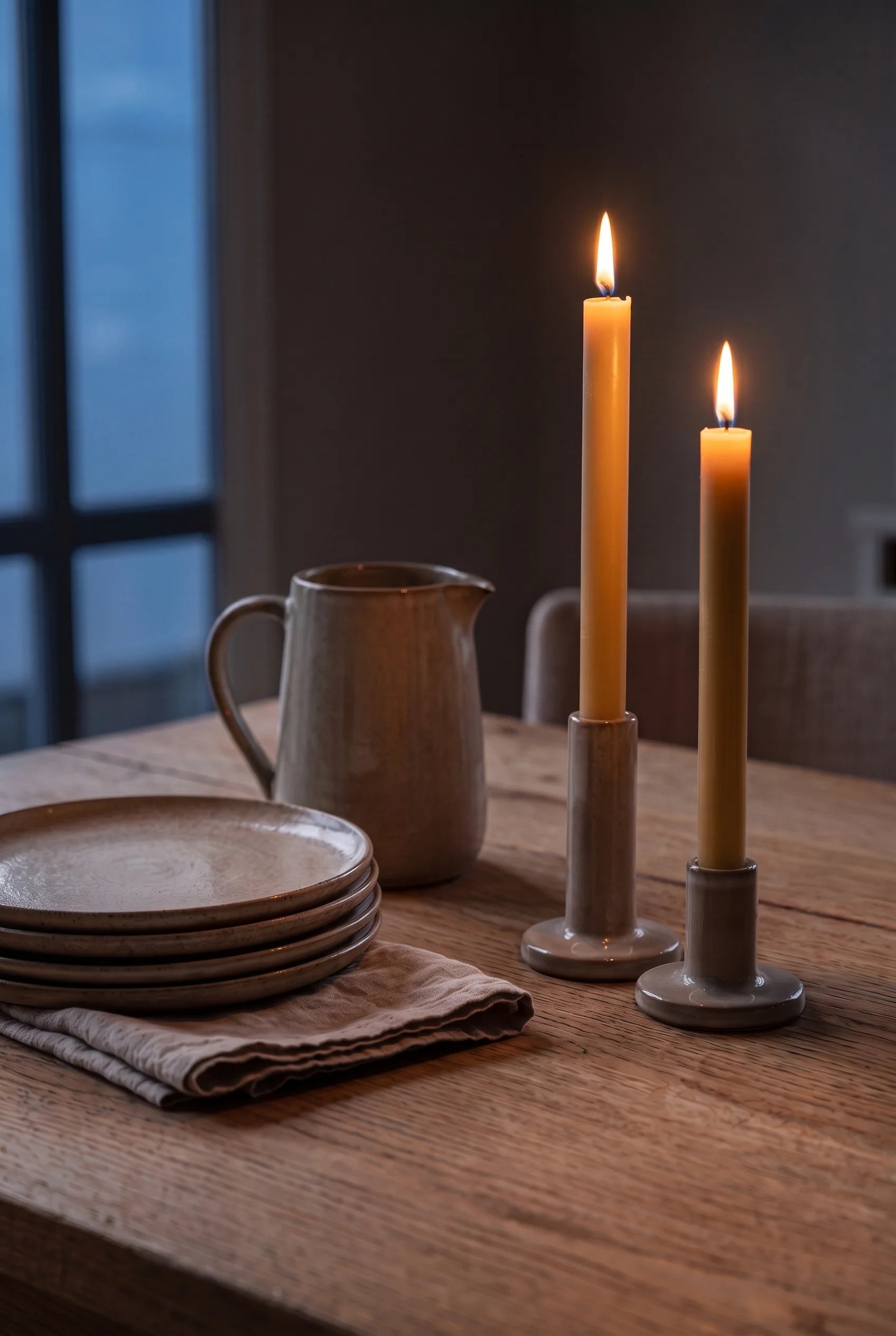 To tændte stagelys i gylden bivoks på anretterbordet om aftenen — flammerne lyser tallerkenstablen op før servering.