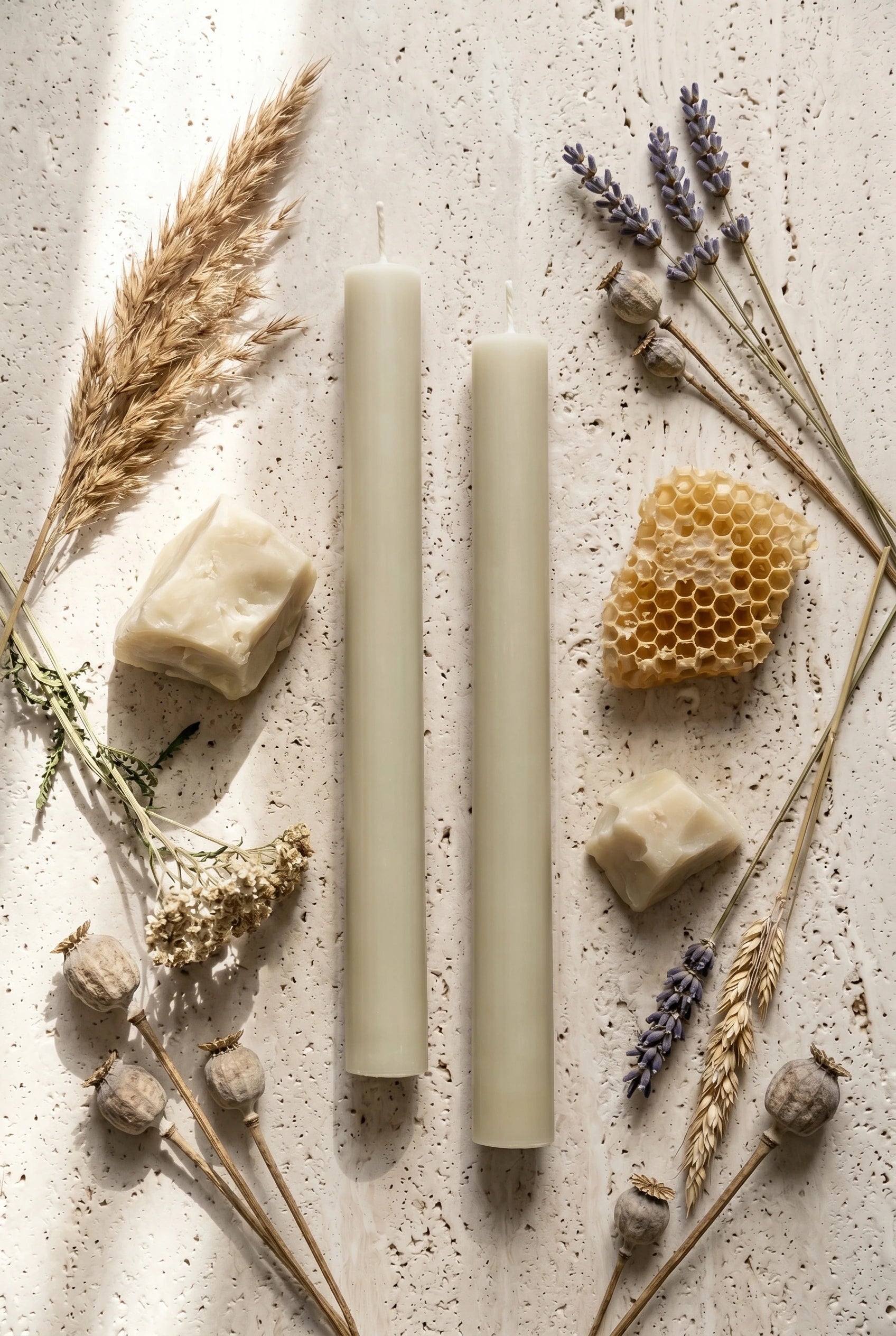 Flatlay top-down af Grenen Råhvid bivoks-stagelys på travertin med tørret tagrør, lavendel, hvede, valmue og rå bivoks-klumper